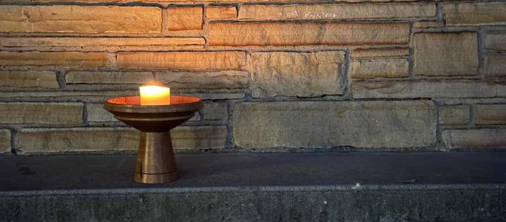 Wooden lit chalice on stone wall. Symbol of Unitarian Universalism. Photo by Peter Poulides.